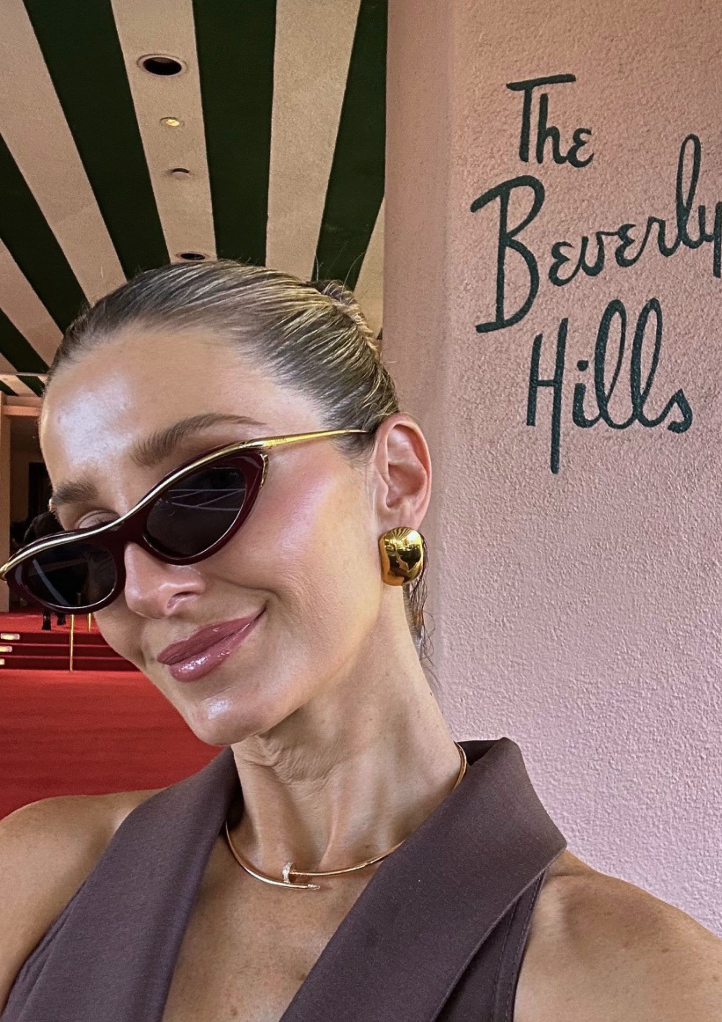 Kate Waterhouse selfie at The Beverly Hills Hotel wearing cat-eye sunglasses, gold sculptural earrings and a slim gold necklace