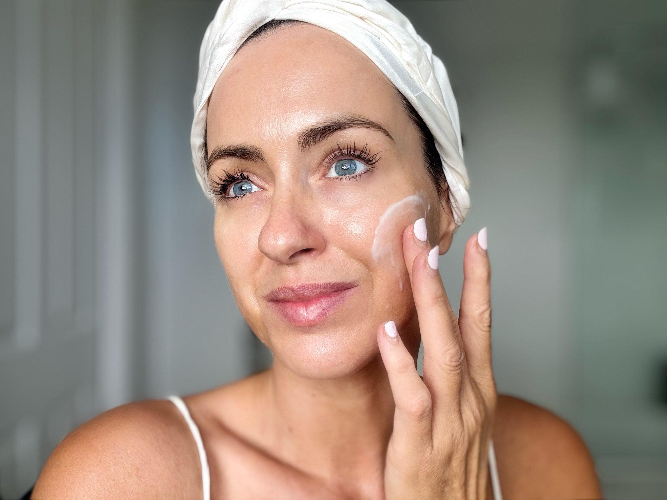 Woman applying water-cream mask by the pool in natural garden setting, wearing spa skincare