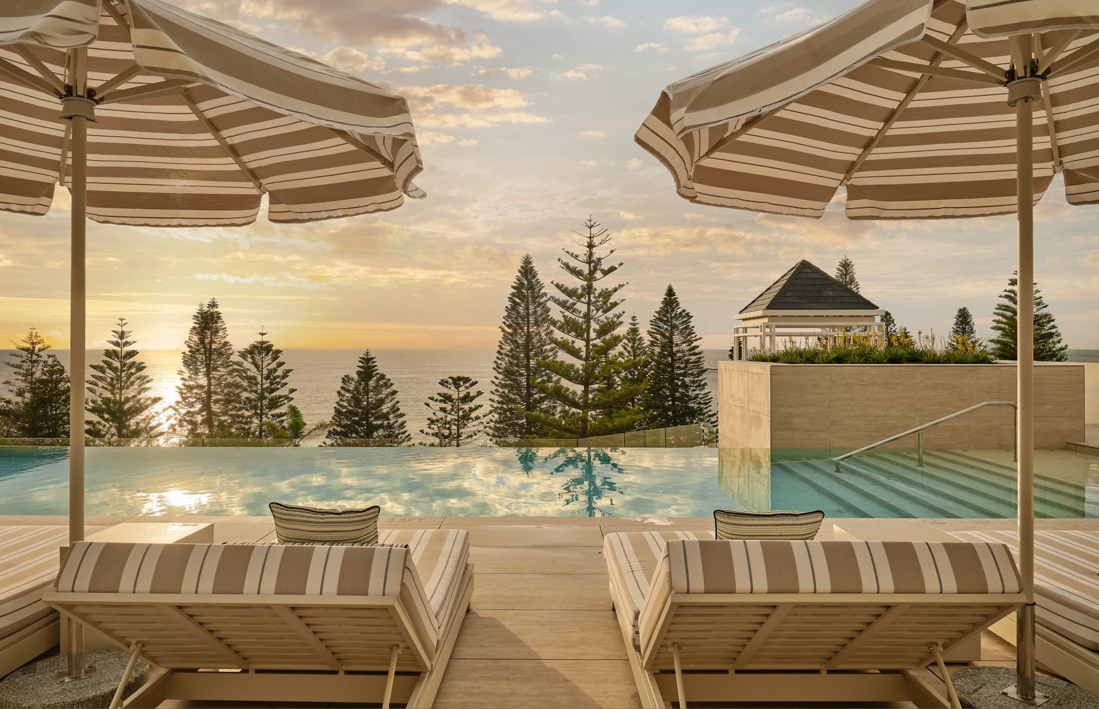 The oceanfront infinity pool at sunrise, striped umbrellas and loungers on the deck, InterContinental Sydney Coogee Beach