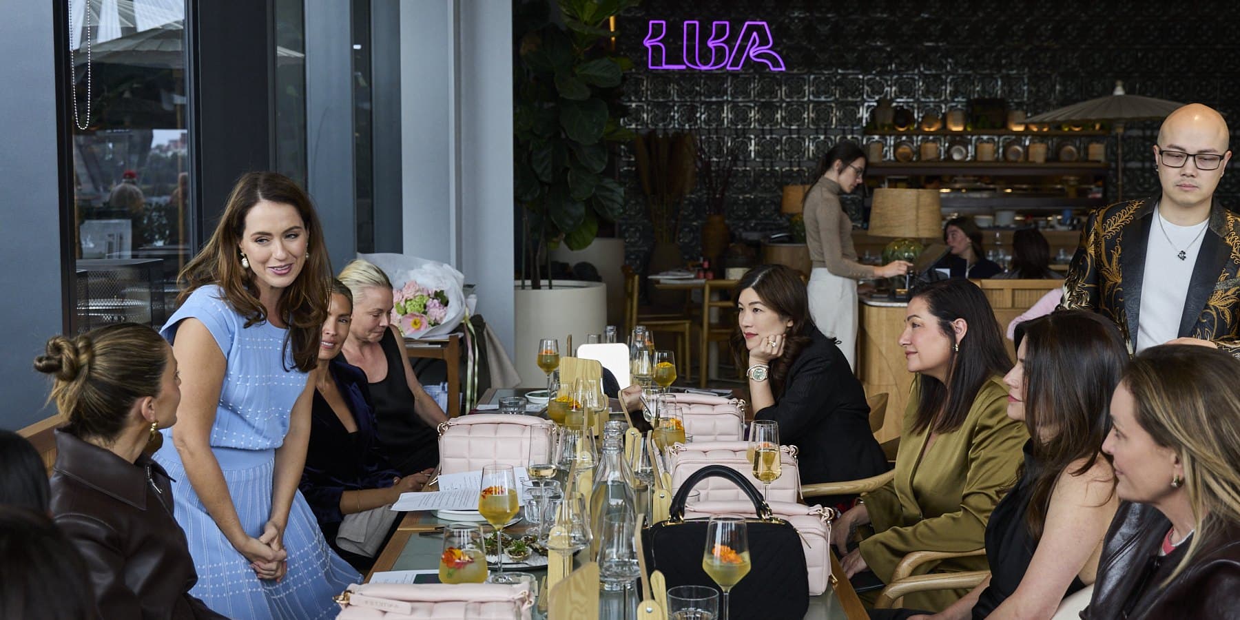Sigourney Cantelo in a blue knit dress with a guest at Lua, Sydney Fish Market, under the neon Lua sign