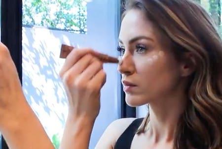 Woman applying contour and highlighter makeup at a restaurant table for sculpted summer skin