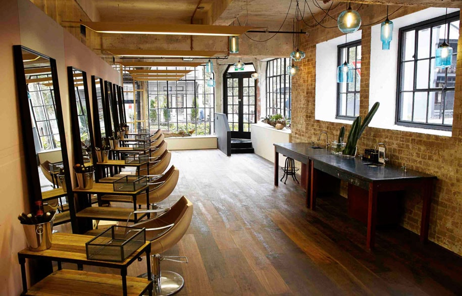 Modern industrial-style hair salon interior with dark wood panels, exposed brick, and low-hanging pendant lights