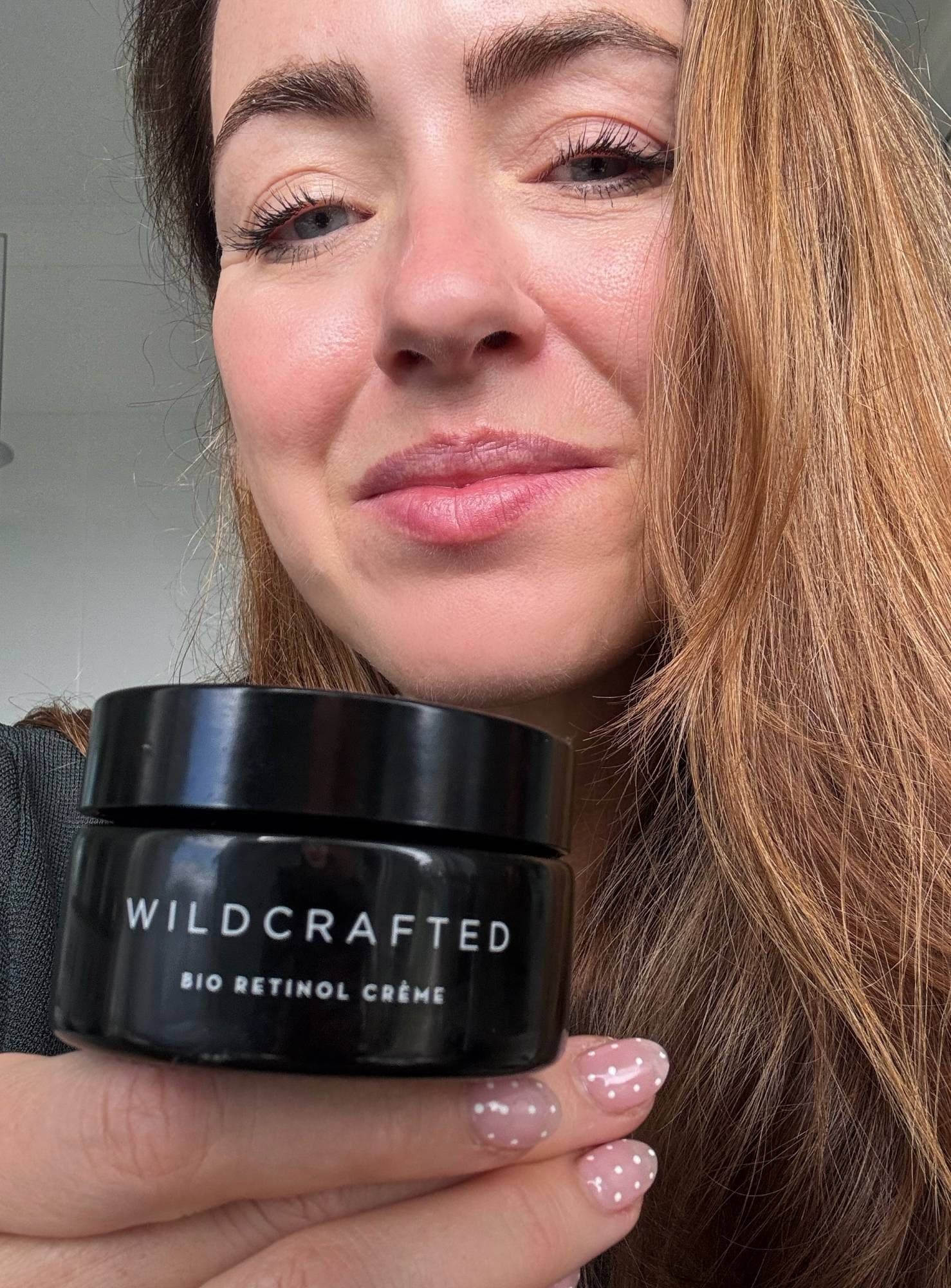 Sigourney holding the Wildcrafted Organics Bio Retinol Crème jar under her chin
