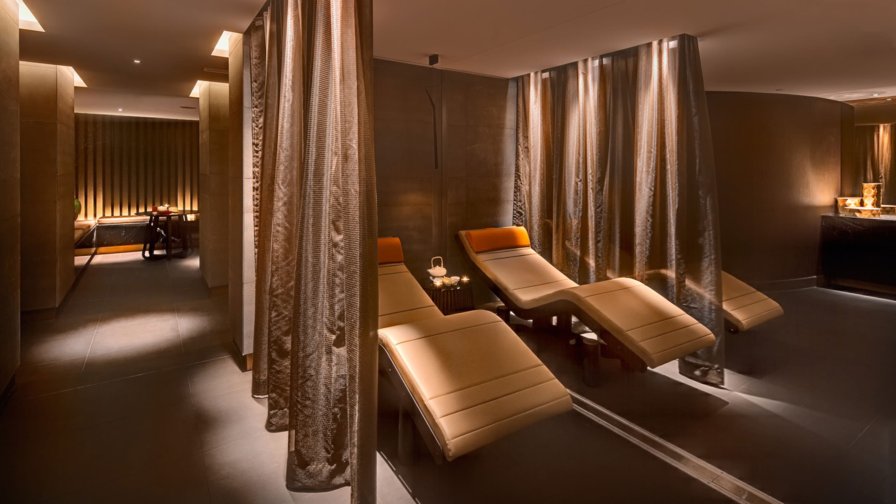 Dimly lit relaxation lounge at The Darling Spa with cream chaise lounges, sheer bronze curtains and warm amber lighting