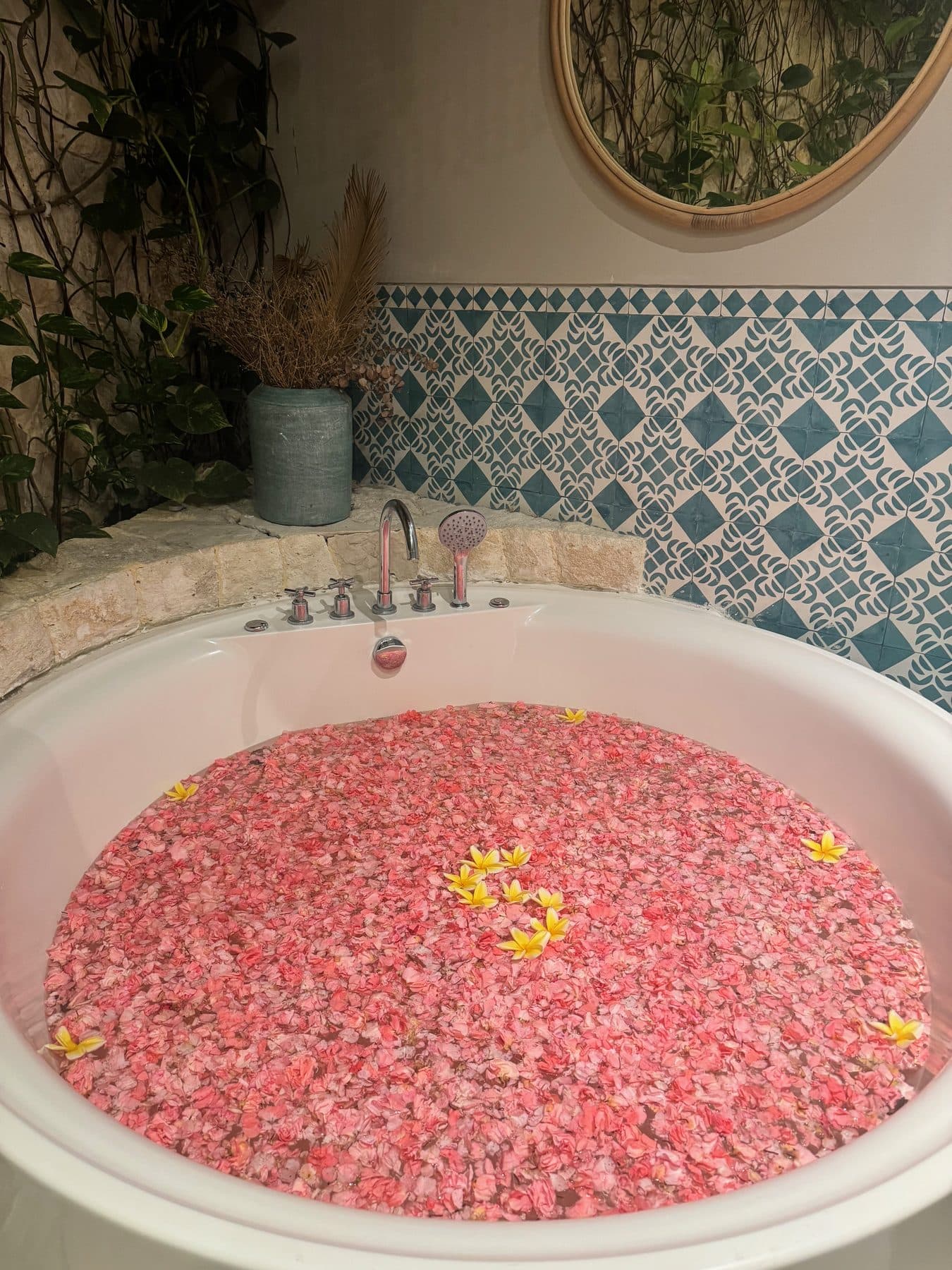 The flower bath at Escape Haven Bali, a round tub filled with pink petals and frangipani against blue Moroccan tiles
