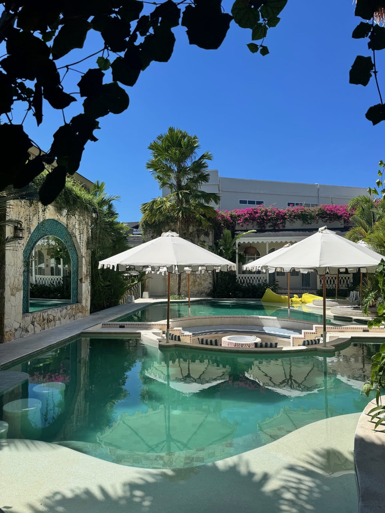 The pool at Escape Haven Canggu, a tiled Moroccan arch and white parasols under bougainvillea
