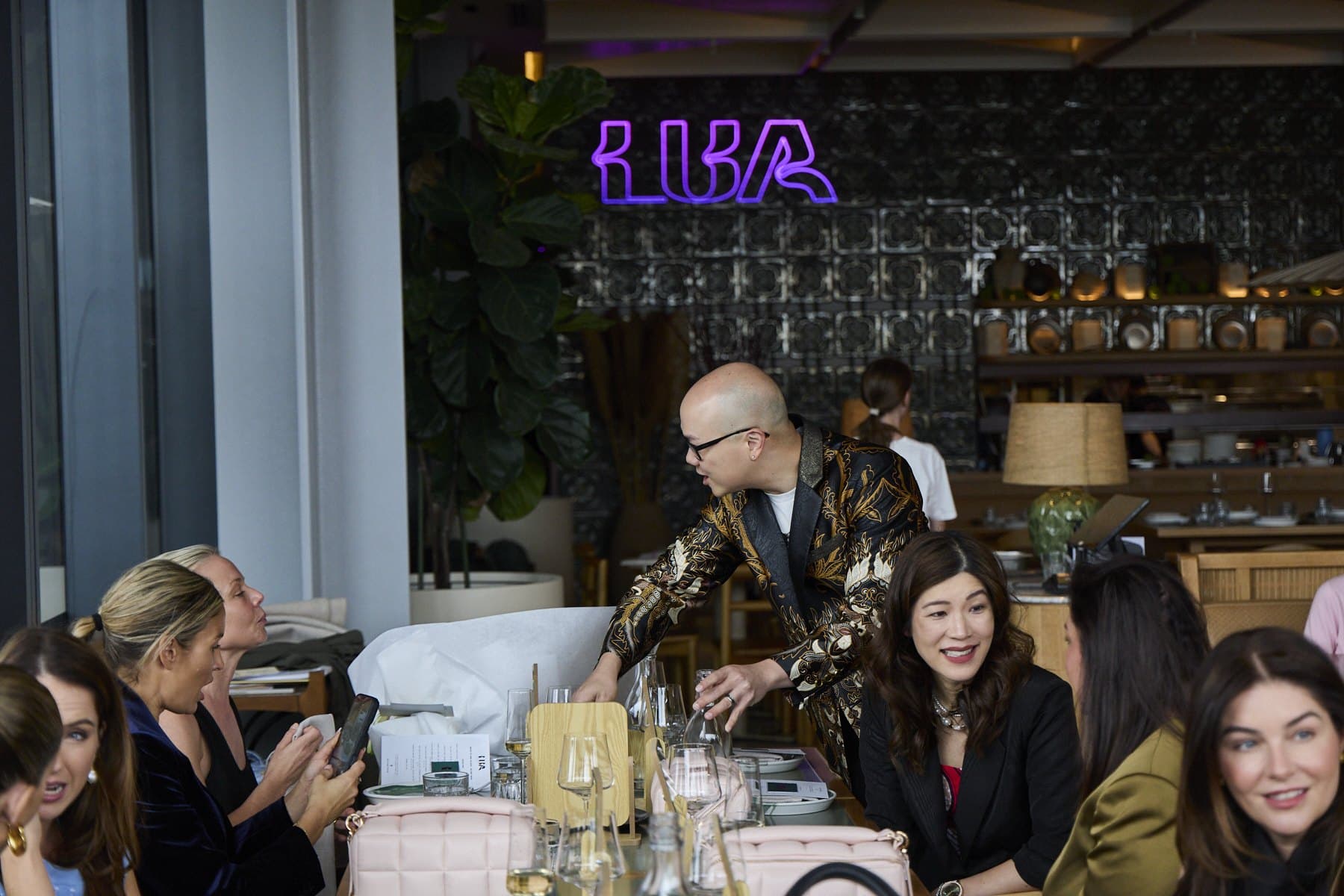 The long table at Lua in full swing, with guests talking and the neon Lua sign behind