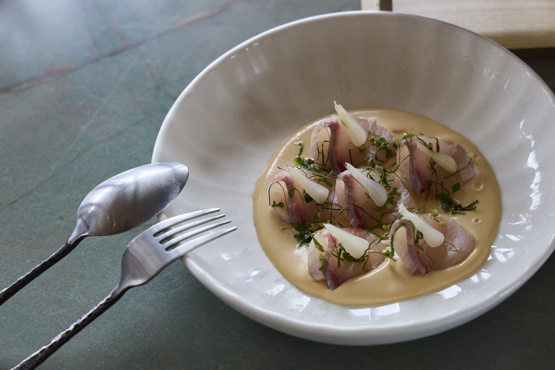 Kingfish crudo in a pale coconut milk sauce with herbs in a white bowl