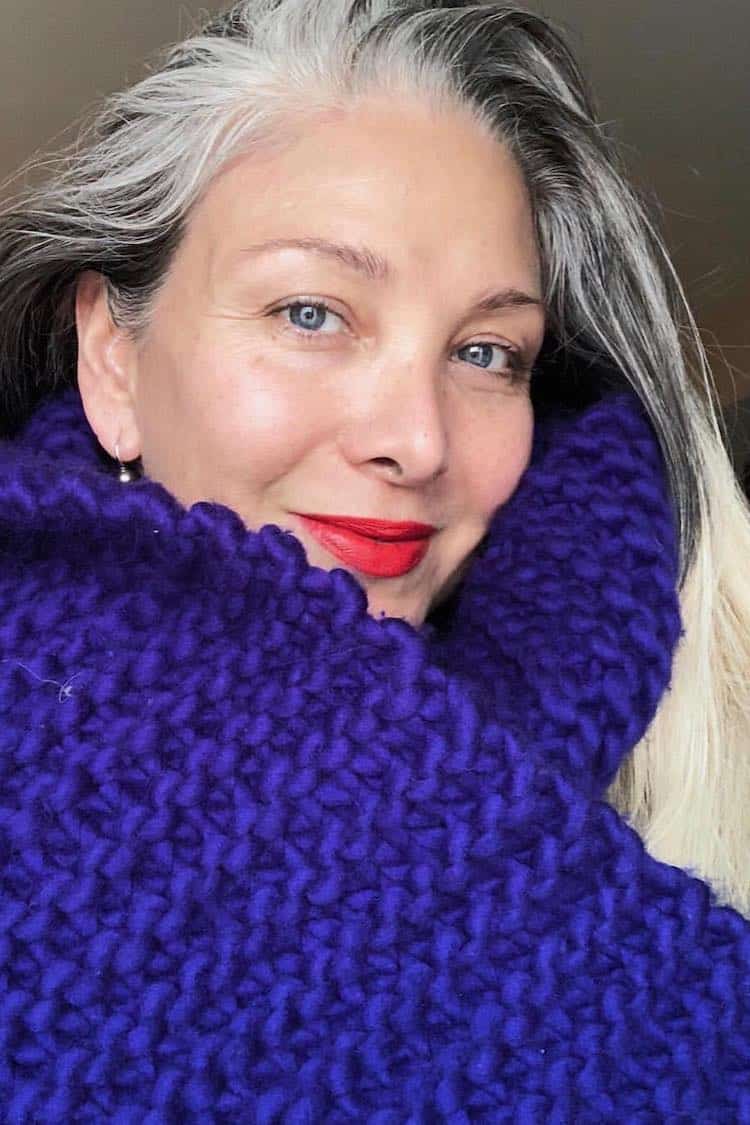 Rose-Marie Swift in a chunky purple knit turtleneck, silver hair loose, wearing red lipstick and smiling