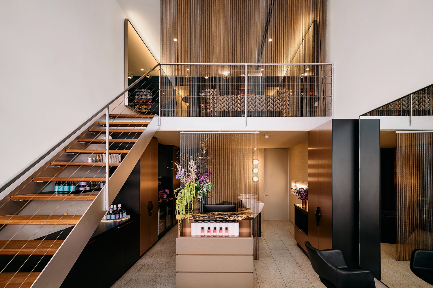 Split-level interior of La Boutique's Darlinghurst salon, with timber staircase and bronze mesh-panelled mezzanine