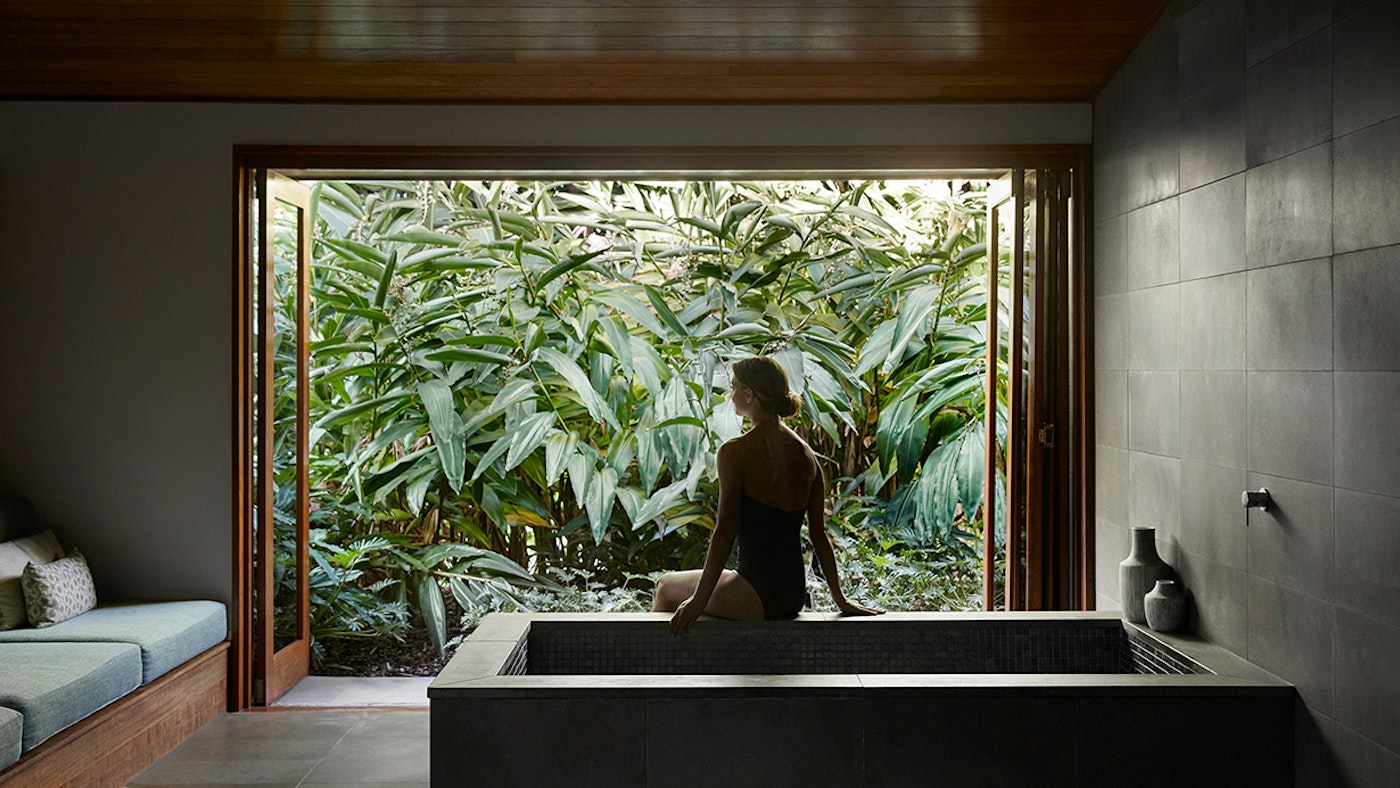 A guest sits at the edge of a private Roman bath overlooking lush rainforest foliage at Spa qualia