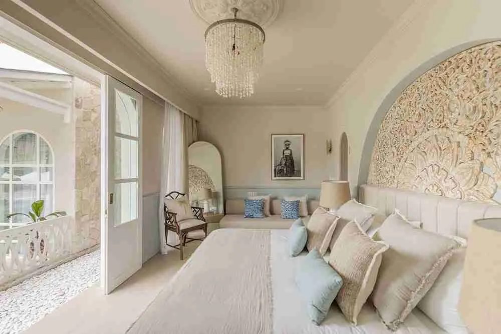 A second goddess room at Escape Haven, cream and pale blue with a carved timber bedhead and doors onto the stone courtyard