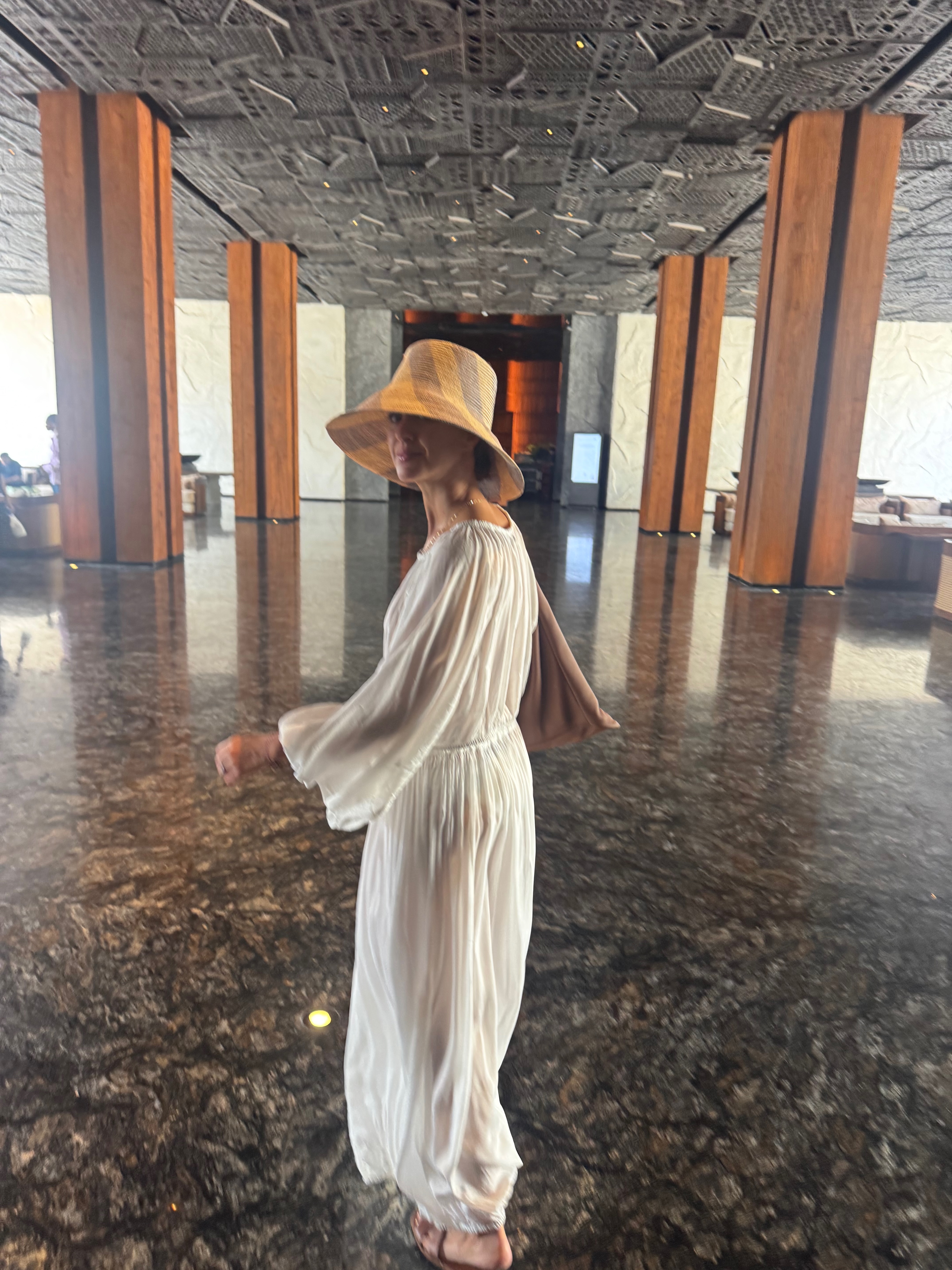 Sigourney arriving in The Meru Sanur lobby — a dramatic space with carved ceilings, sculptural lighting and lush greenery