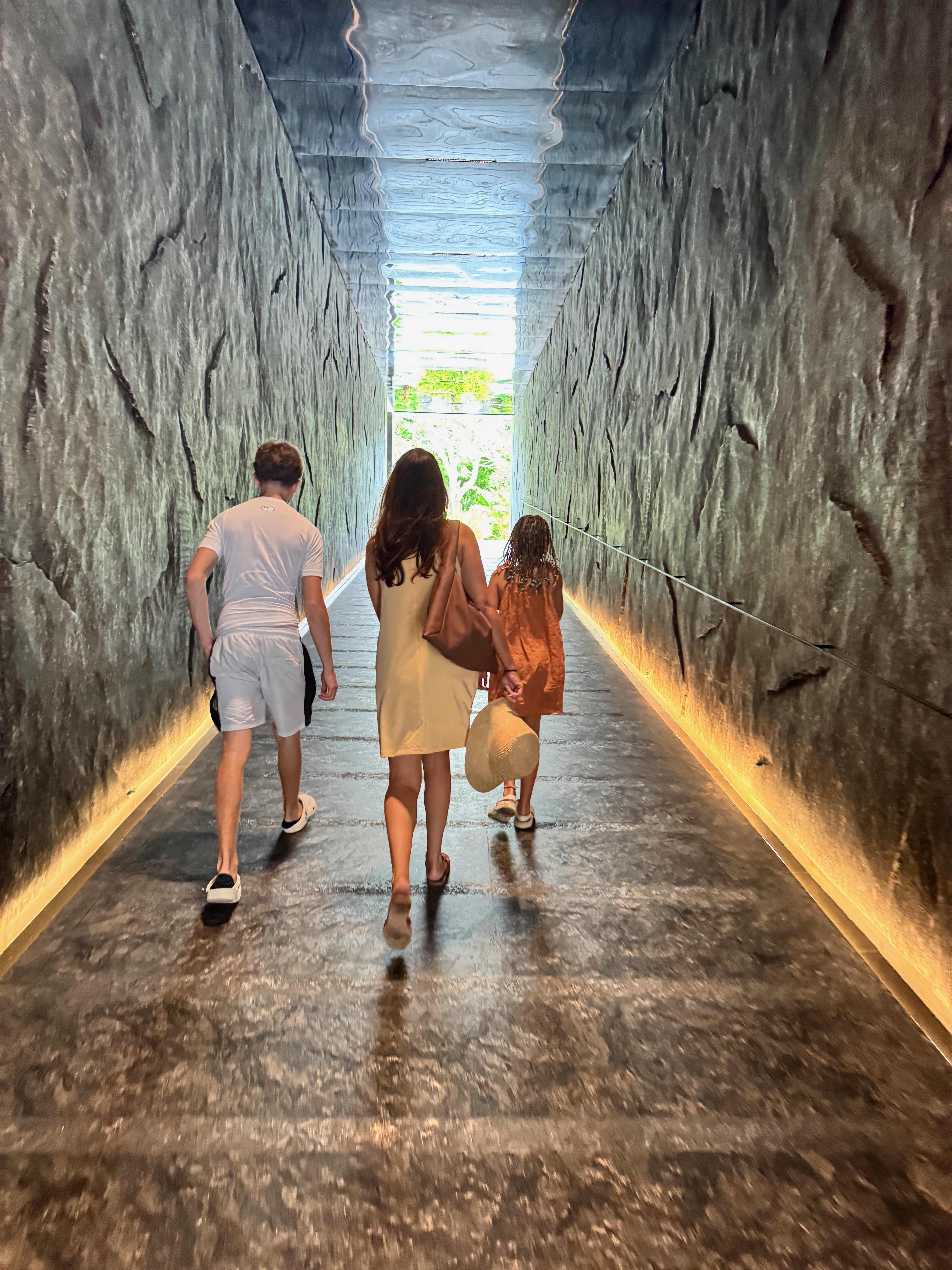 The dramatic underground tunnel entrance to The Meru Sanur, with rough-surfaced marble walls, a glossy reflective floor and sculpture galleries on either side