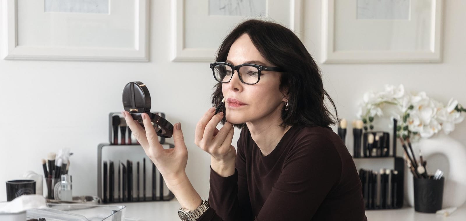 Rae Morris makeup brushes in a Diptyque Baies candle vessel with a brush stand and white orchids behind