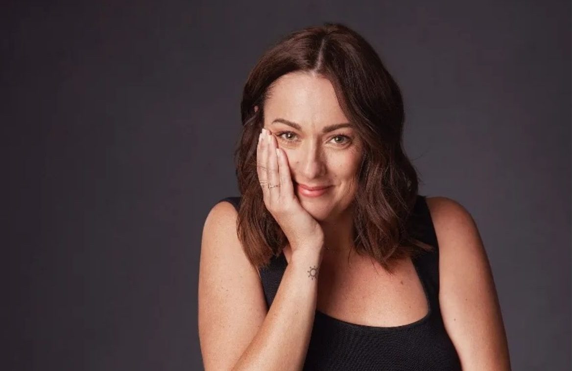 Celeste Barber resting her cheek on her hand, smiling softly against a charcoal backdrop